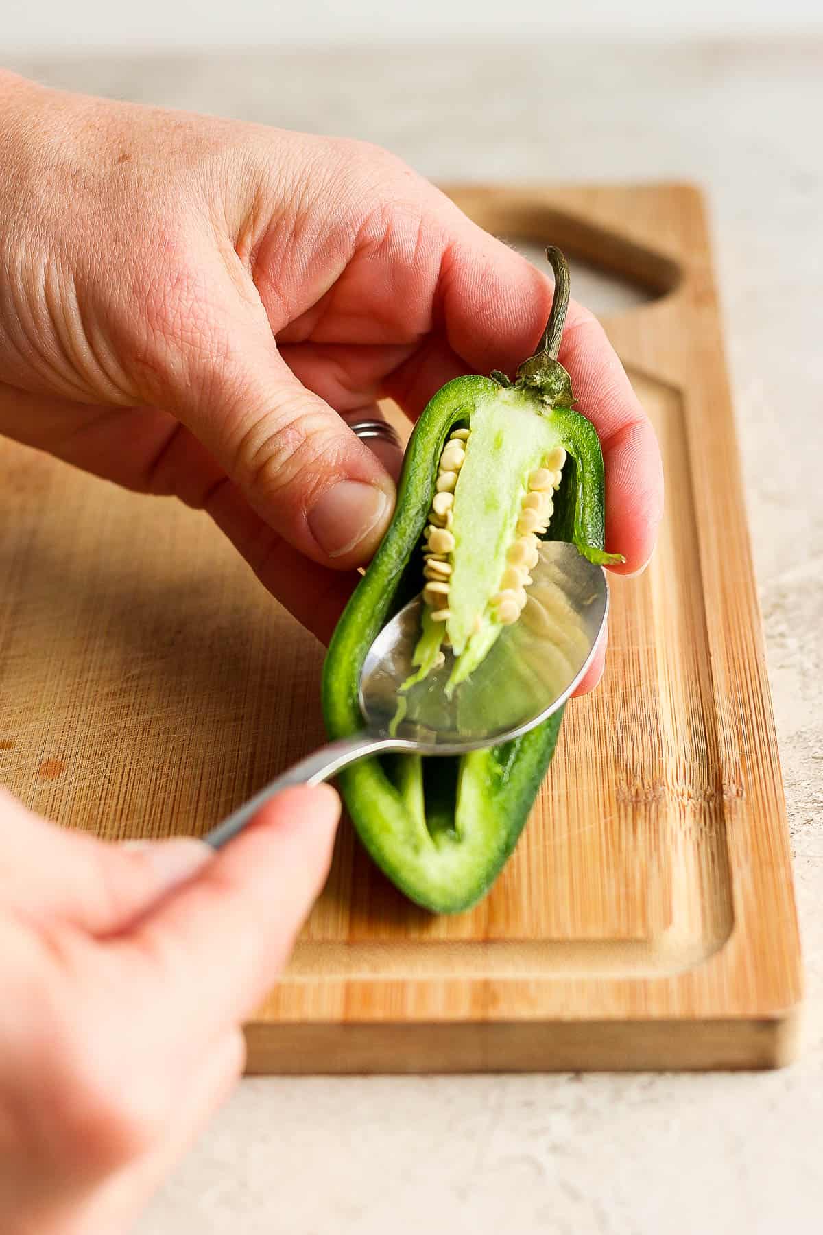 The seeds and membrane of a jalapeño pepper sliced in half being removed.