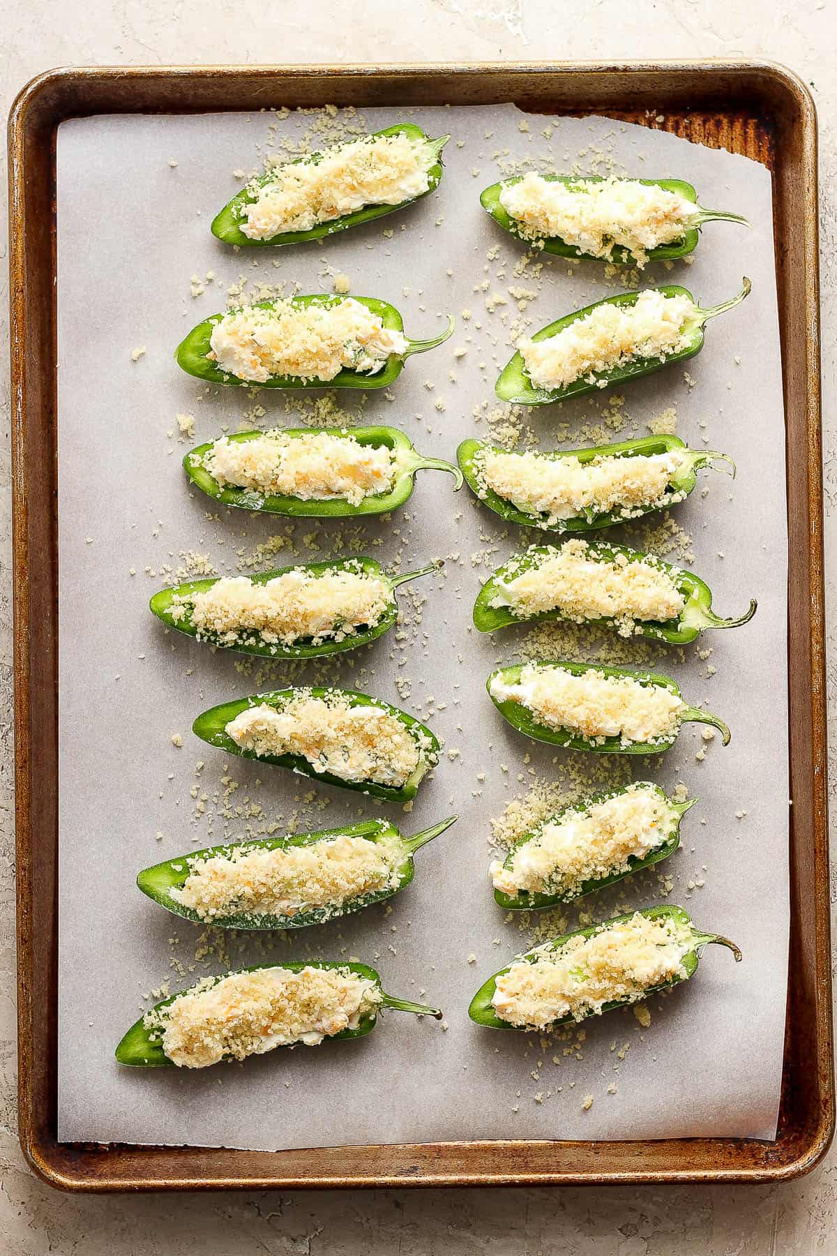 Unbaked jalapeno poppers on a baking sheet lined with parchment paper.