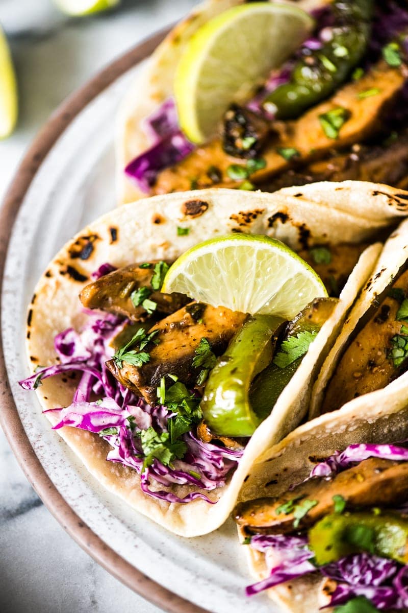 Close up photograph of mushroom tacos filled with red cabbage slaw, sauteed portobello mushrooms, sauteed bell peppers and garnished with cilantro.