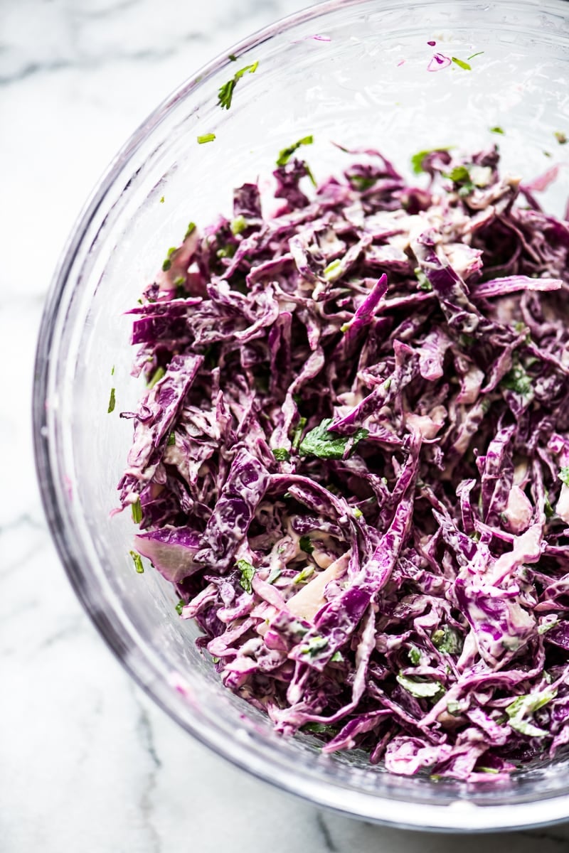 Shredded red cabbage in a large bowl with mayo and chopped cilantro for vegetarian tacos topping