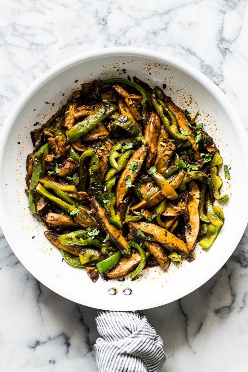 Sauteed portobello mushrooms with bell peppers in a white skillet.