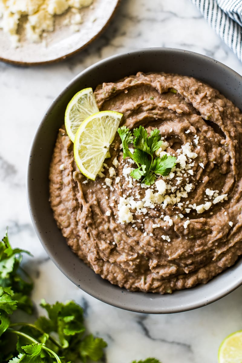Easy refried beans recipe in a serving bowl with cotija cheese and cilantro