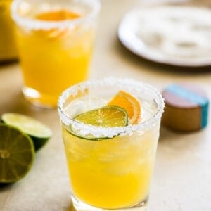 Skinny margarita cocktail glass garnished with sliced lime and orange.