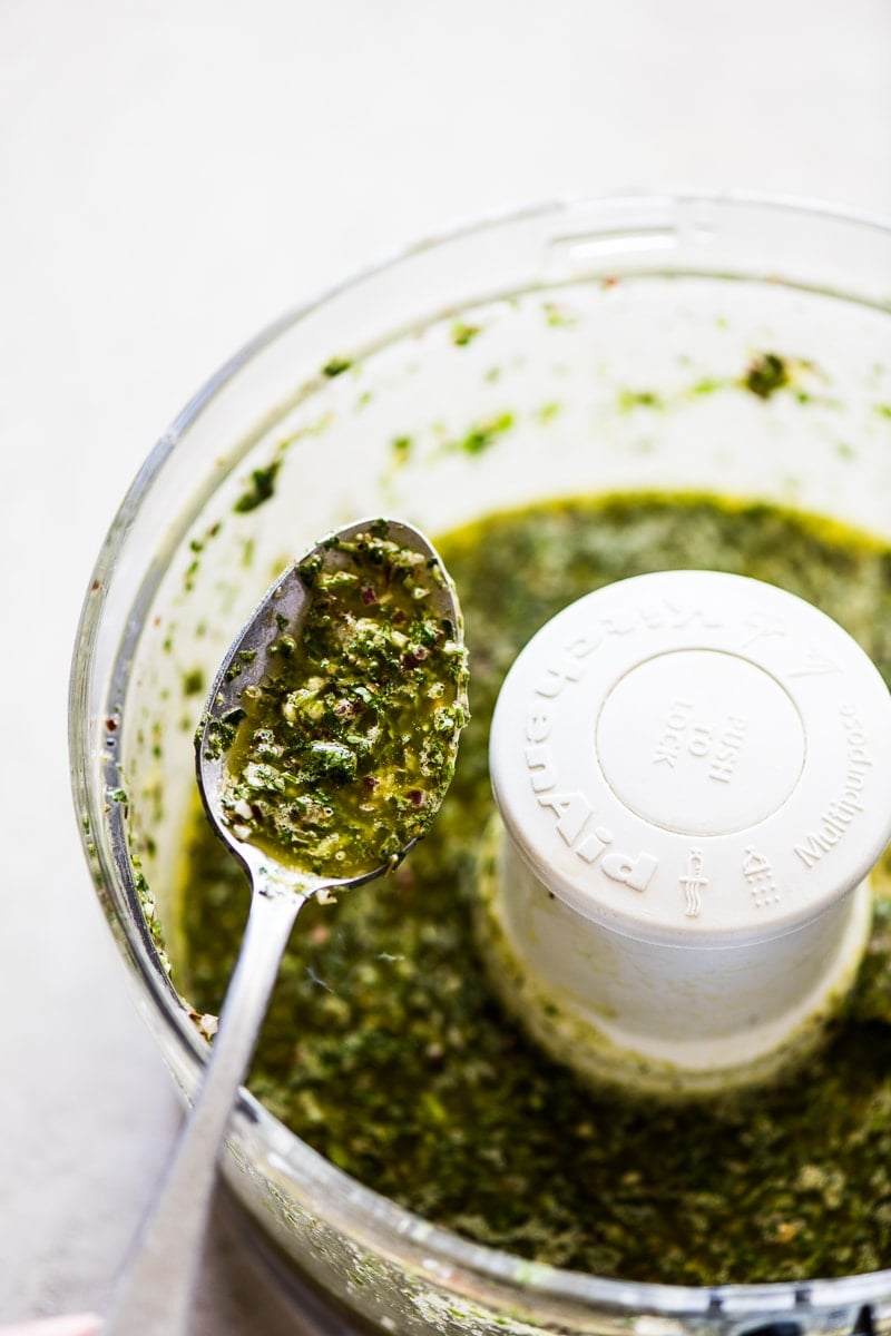 Chimichurri on a spoon next to a food processor.
