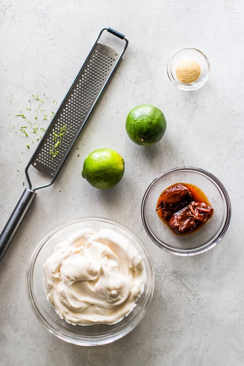 Ingredients for chipotle sauce on a table. Includes mayonnaise, chipotle peppers, limes, garlic and lime zest.