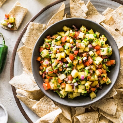 Pineapple salsa in a bowl surrounded by tortilla chips.