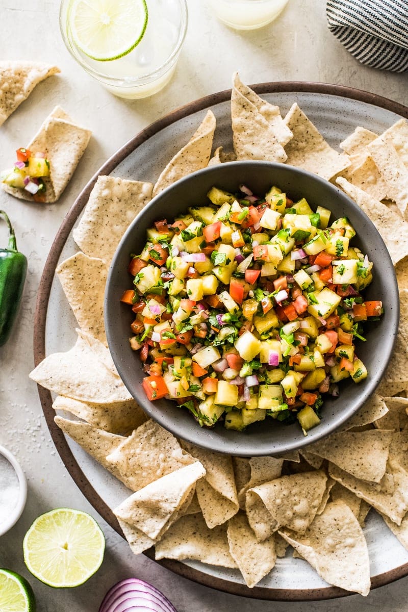 Pineapple salsa in a grey bowl  served with a platter of tortilla chips.