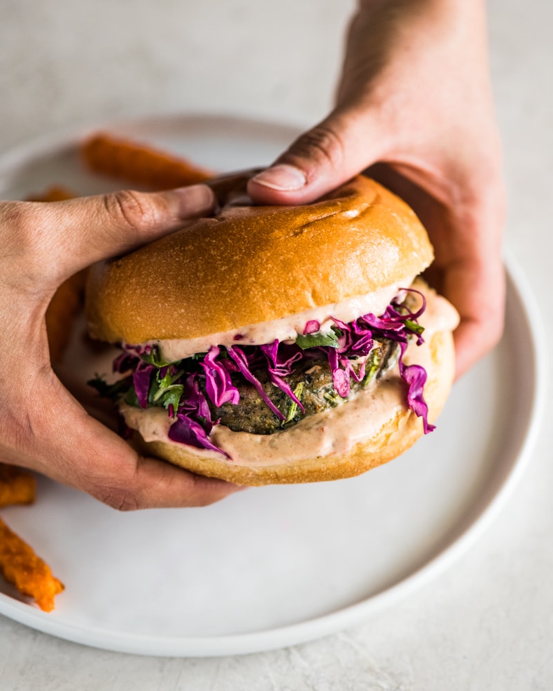 Hands holding a grilled turkey burger made with chipotle mayo and red cabbage slaw.