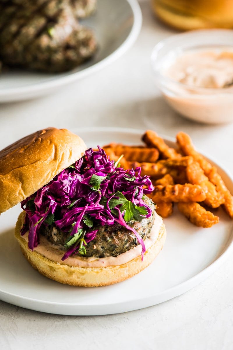 A grilled turkey burger sitting on a hamburger bun topped with chipotle lime mayo and a red cabbage slaw.