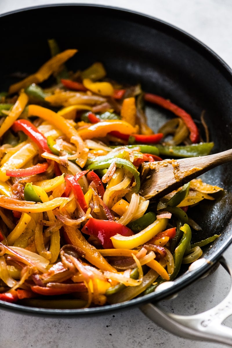 Sauteed peppers and onions in a black nonstick skillet.