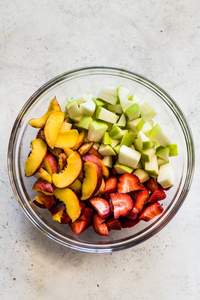 A large clear bowl filled with chopped green apples, sliced peaches and sliced strawberries.
