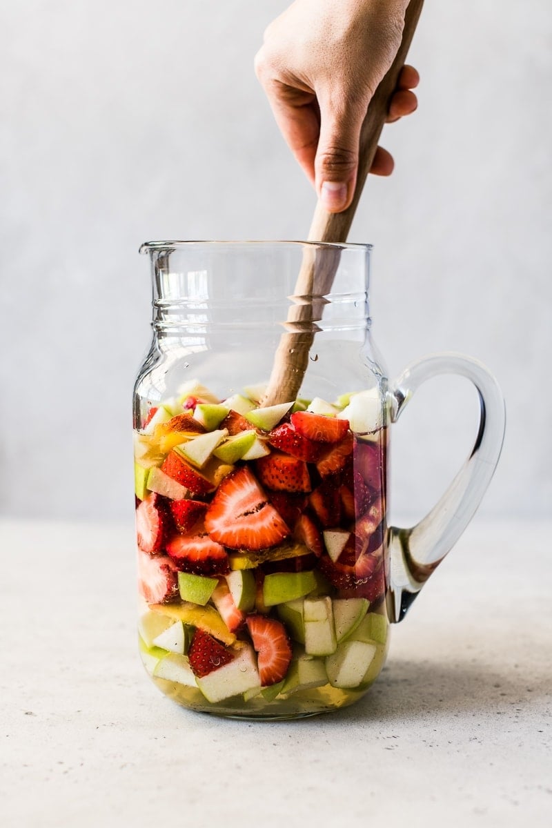 White sangria in a pitcher with strawberries, peaches and apples.