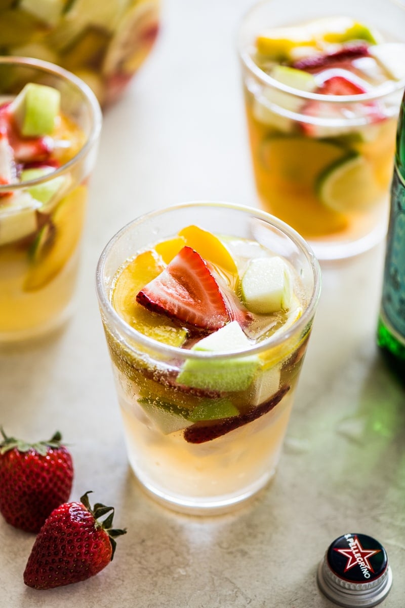 White wine sangria in a clear glass topped with sliced strawberries and summer fruit.