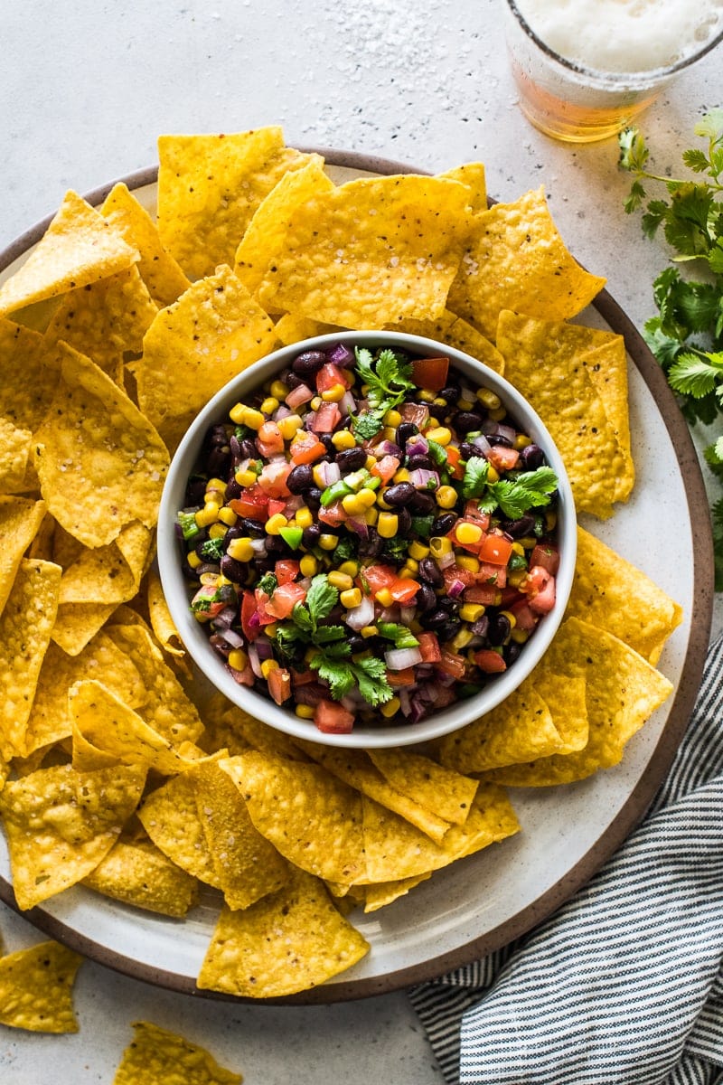 Black bean and corn salsa in a white bowl surrounded by tortilla chips.
