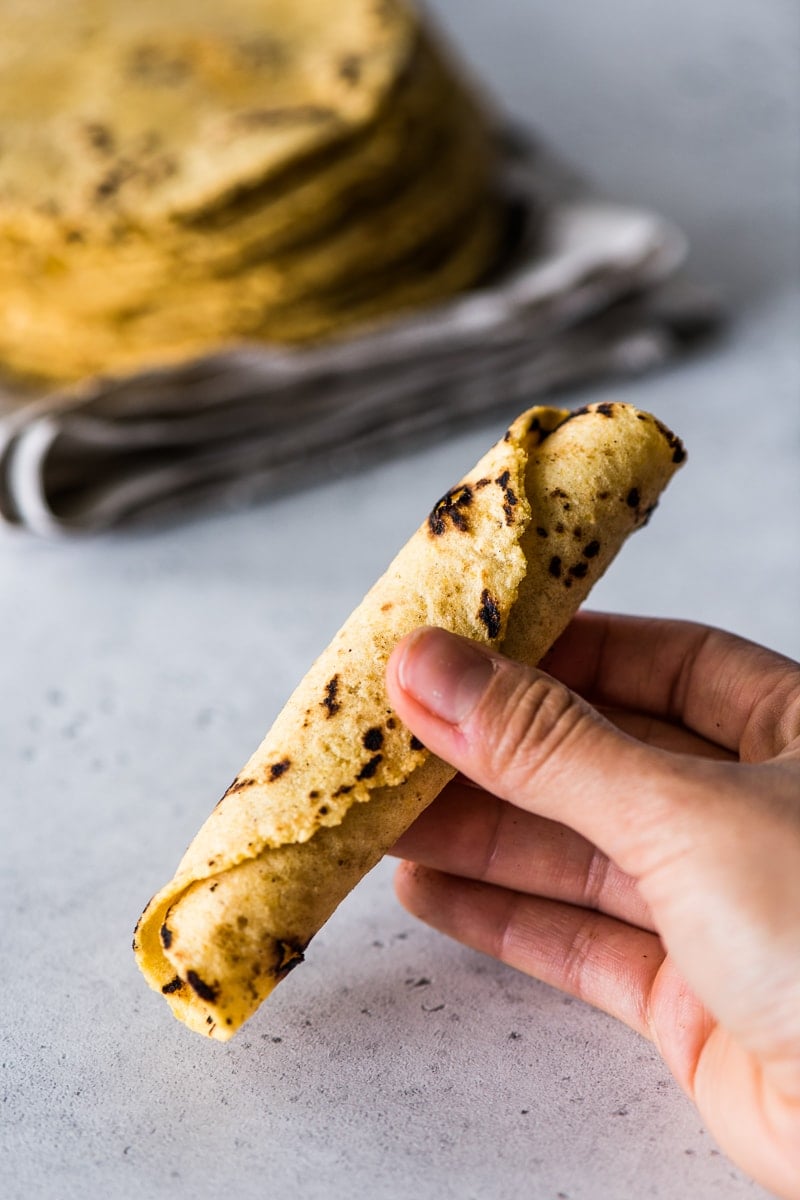 Rolled corn tortilla being held in a hand.