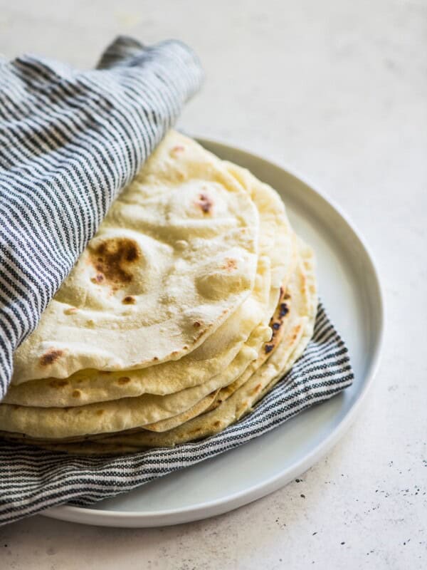 Flour tortillas in between a striped kitchen towel on a white plate.