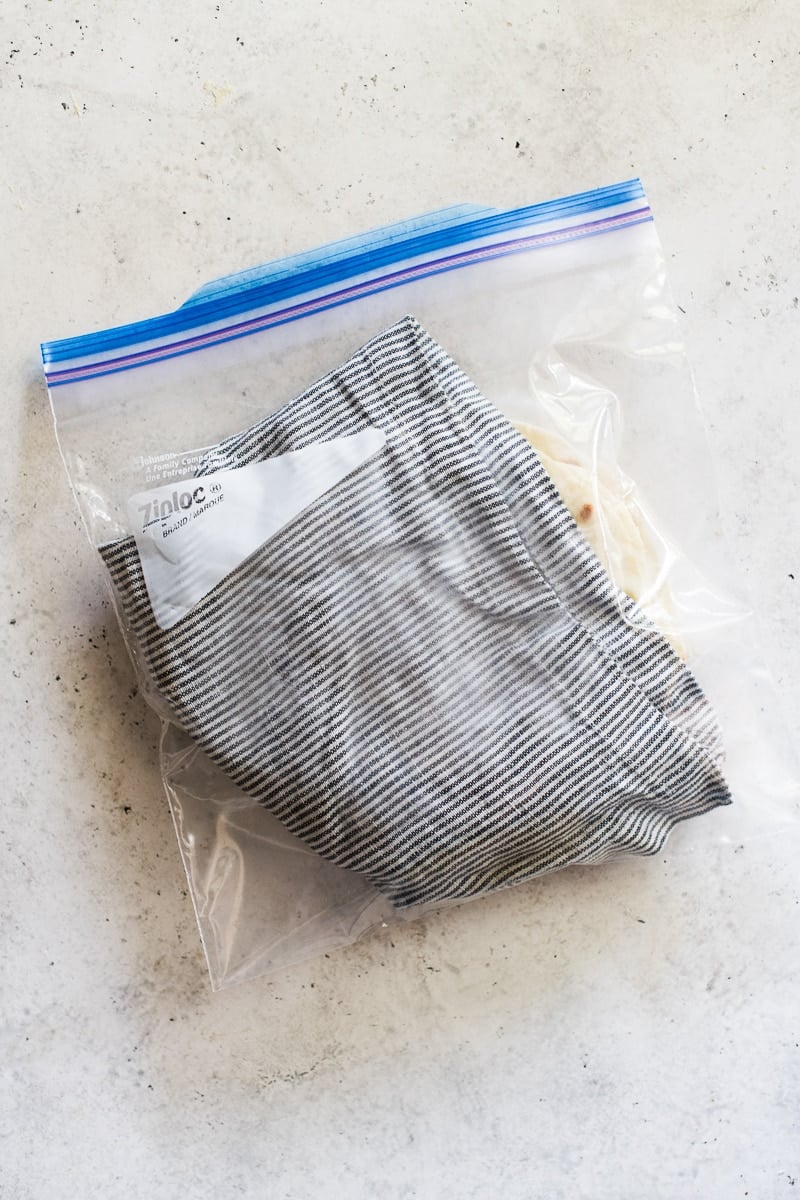 Flour tortillas wrapped in a kitchen towel and then placed into a gallon-sized zip-top plastic storage bag.