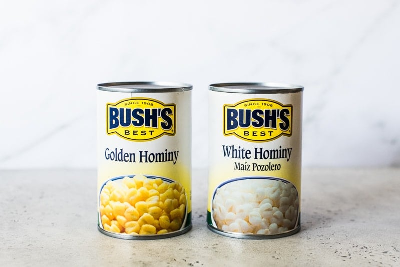 Two cans of different types of hominy. One is golden hominy and one is white hominy.