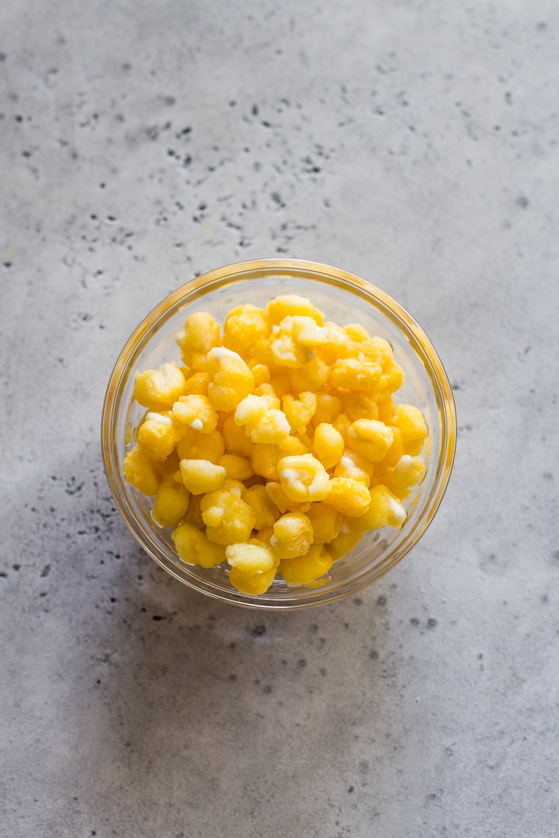 Golden yellow hominy in a small glass bowl.