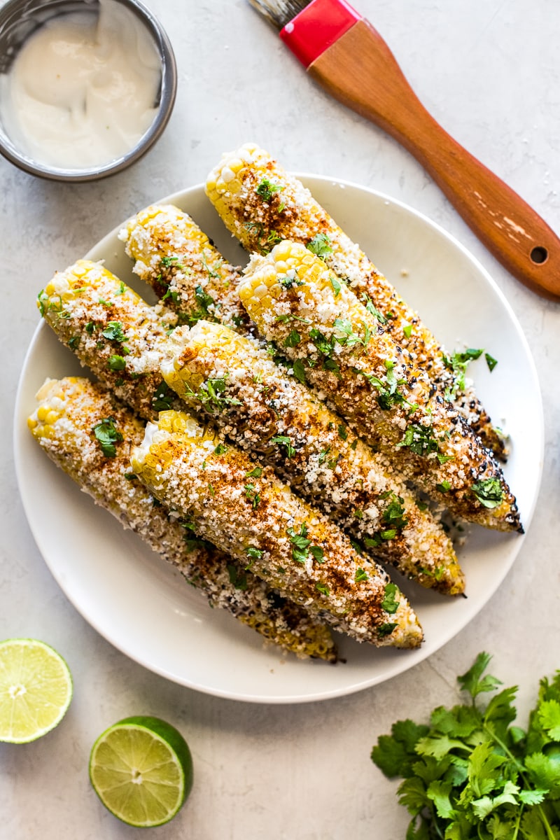  Maïs de rue mexicain sur un plateau blanc entouré de limes, de coriandre et de mayonnaise.