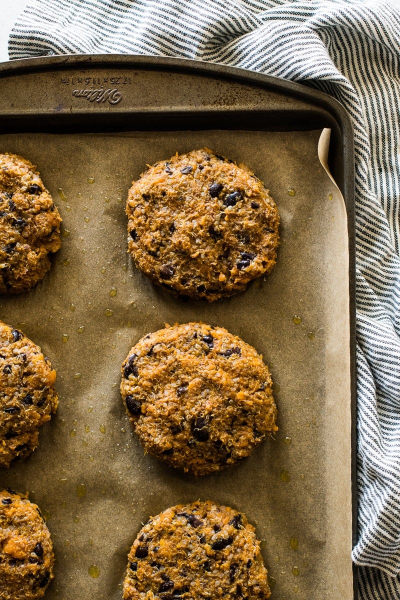 Vegan black bean burgers on a large baking sheet lined with parchment paper.