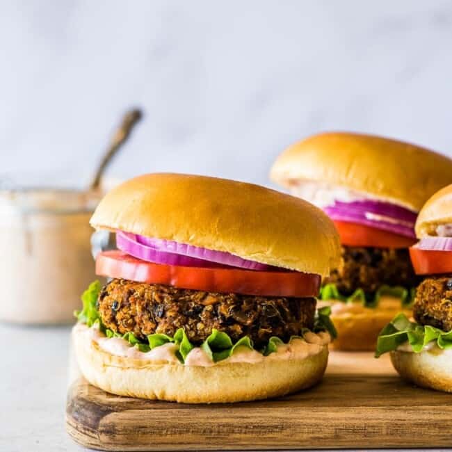 Black Bean Burger on a wooden board with mayo, tomatoes, and lettuce.