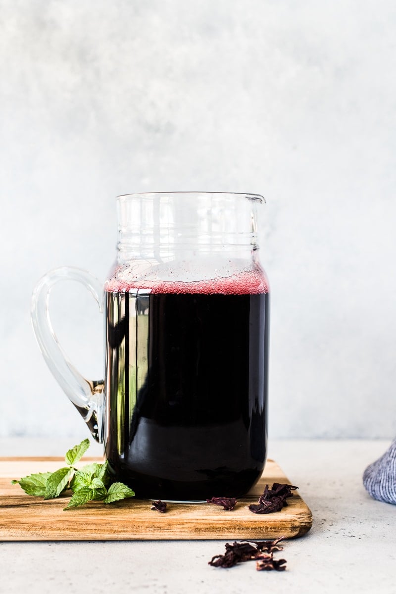 A pitcher of Agua de Jamaica next to some dried hibiscus flowers.