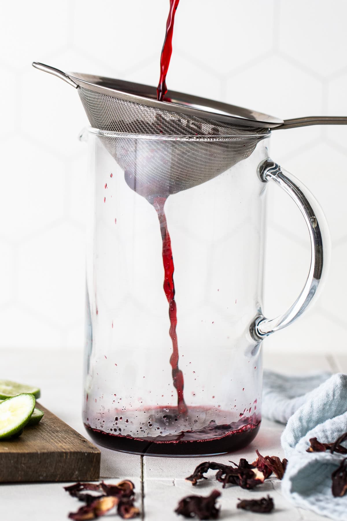 Hibiscus tea being poured through a strainer and into a large pitcher.