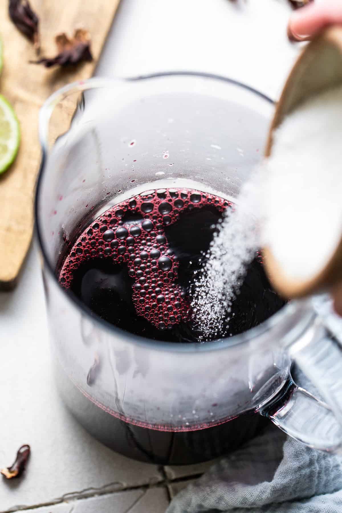 Sugar being poured into a pitcher of agua de jamaica to sweeten it.