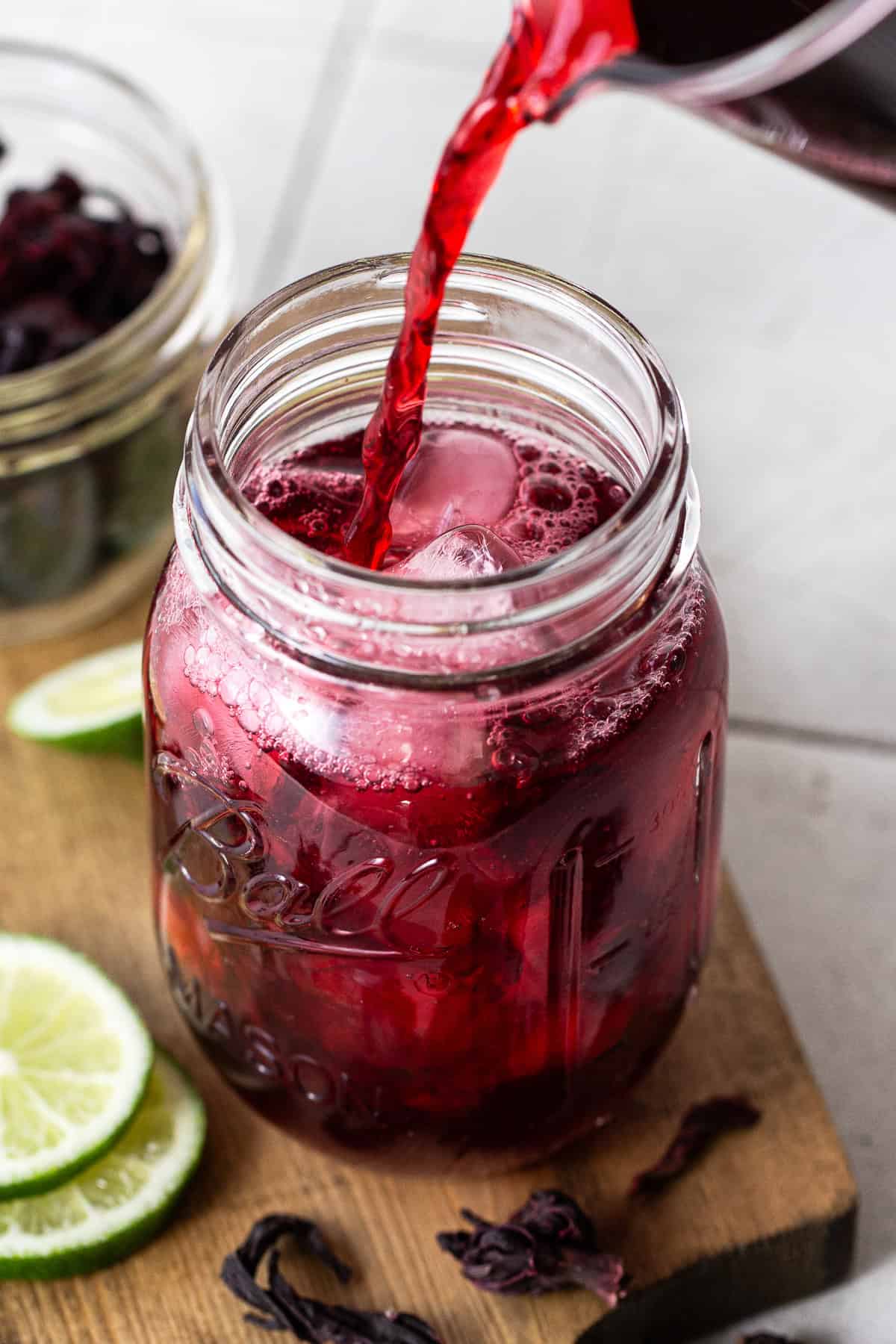 Jamaica drink being poured into a tall glass with ice.