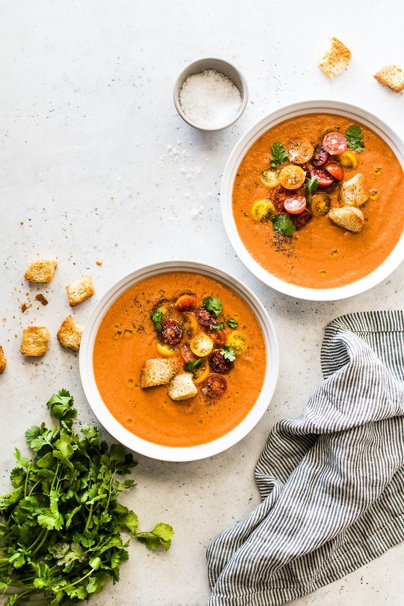 Two white bowls filled with summer gazpacho topped with croutons and a drizzle of olive oil.