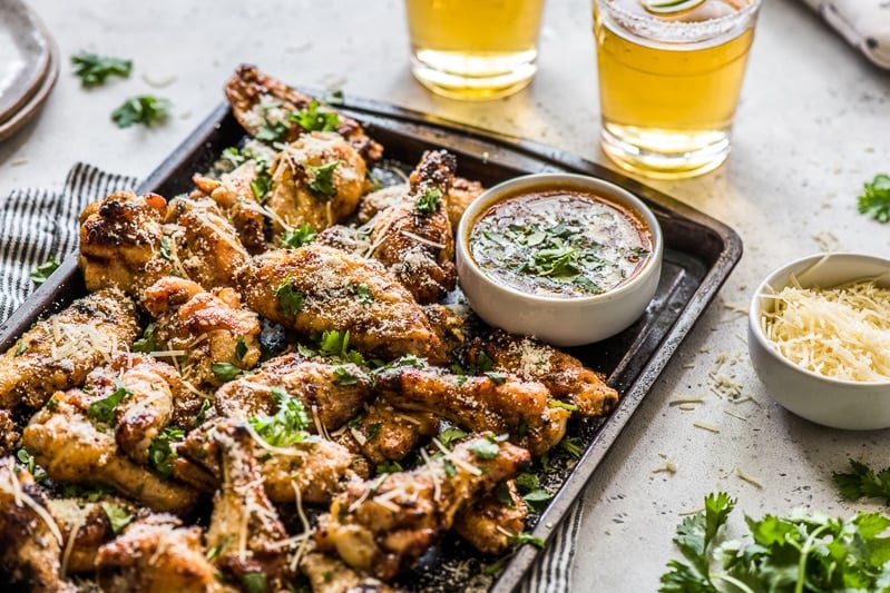 Grilled chicken wings on a serving tray with a side of garlic parmesan sauce.