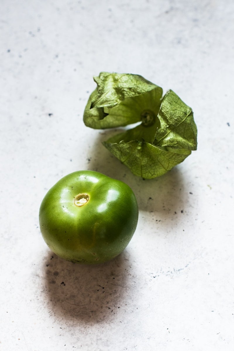 One tomatillo on a white table with the skin and husk removed.