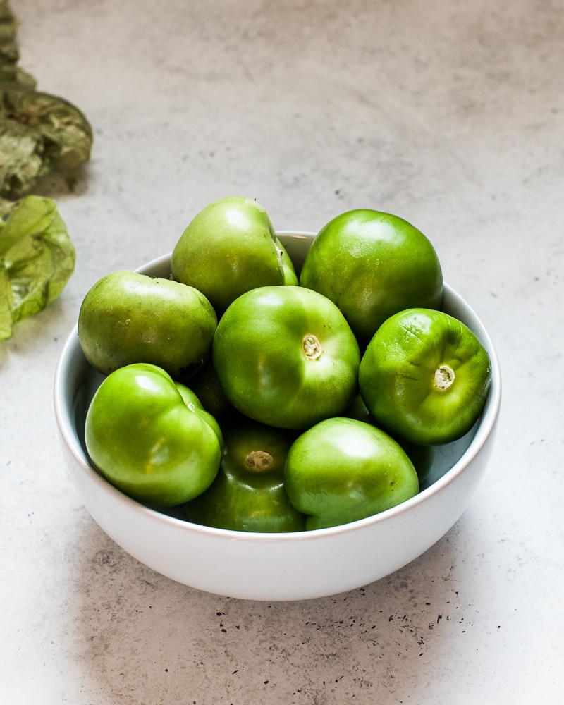 Green tomatillos in a white bowl with the skin and husk removed.