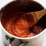 An easy arrabiata sauce in a pot being stirred by a wooden spoon.