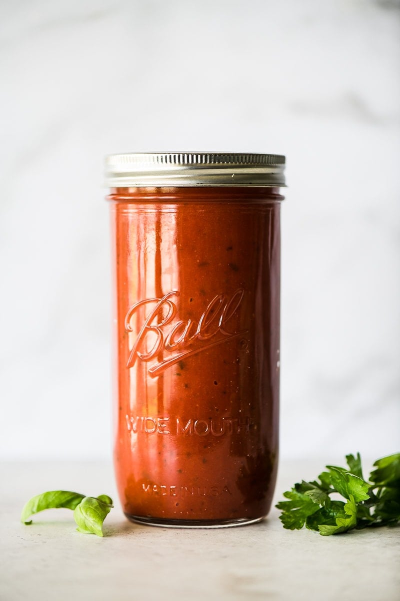 Arrabiata sauce in a glass jar next to fresh basil and parsley.