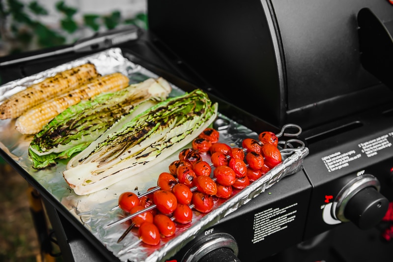 A plate of grilled lettuce, tomato skewers and corn on the cob.