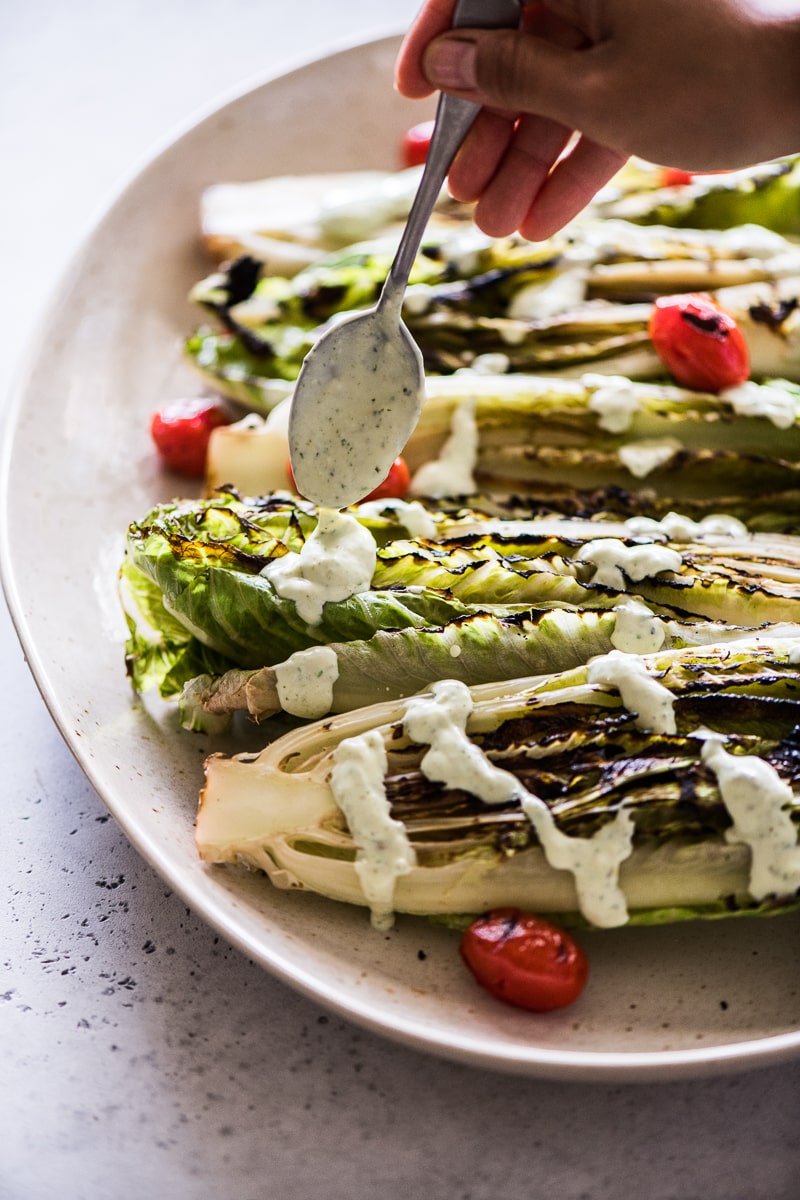 Homemade jalapeno ranch being drizzled on top of grilled romaine lettuce.