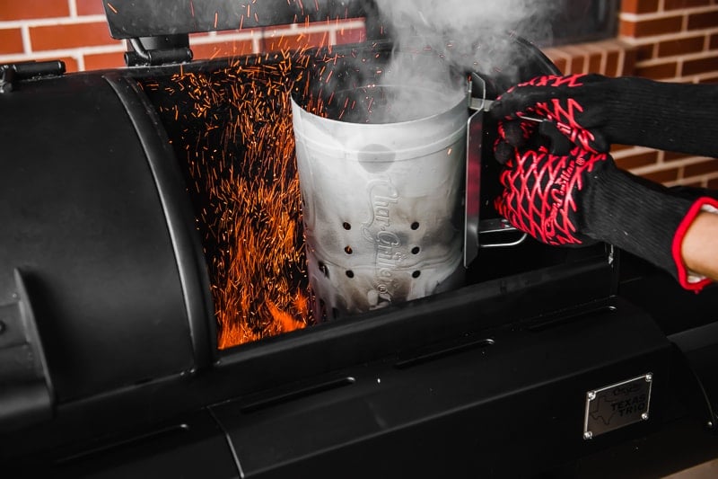 Lit charcoal being dumped into a grill from a chimney starter.