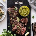 Thinly sliced grilled skirt steak on a cutting board topped with cilantro pesto