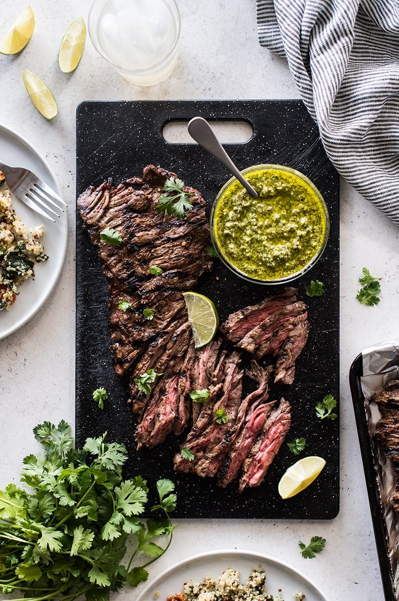 Thinly sliced grilled skirt steak on a cutting board topped with cilantro pesto.