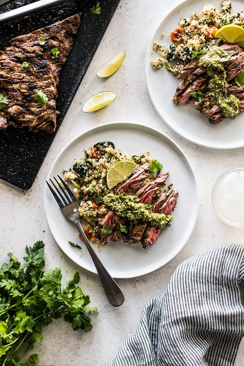 Grilled skirt steak slices on a plate of quinoa topped with cilantro pesto