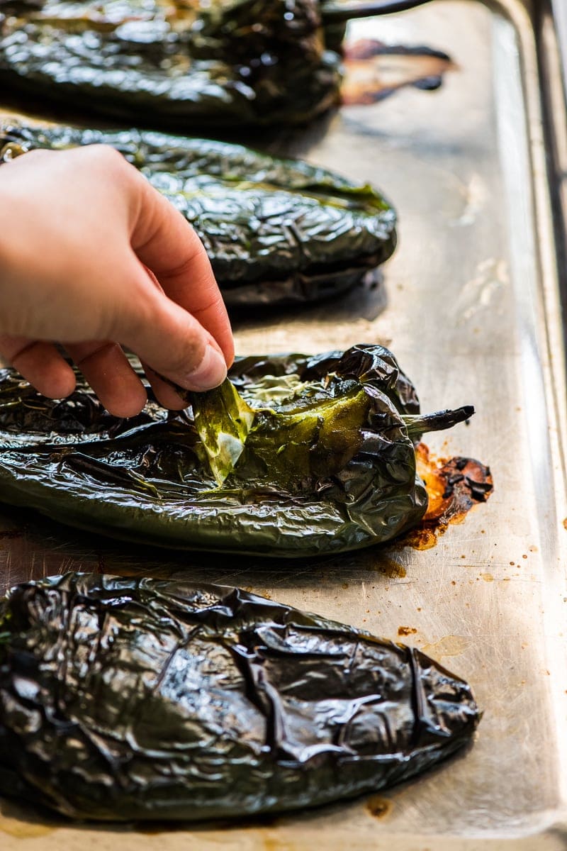 A hand peeling off the skin of a roasted poblano pepper.