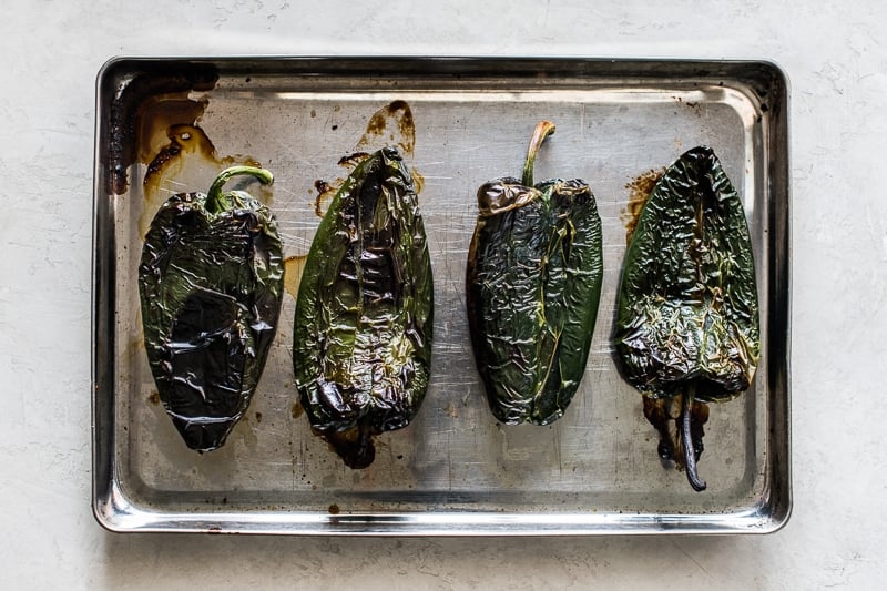 Roasted poblano peppers on a large baking sheet.