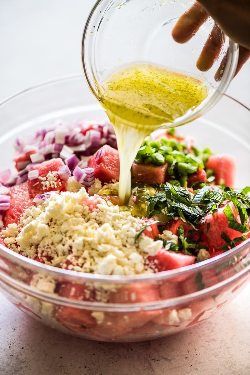 Lime dressing being poured in a bowl of watermelon salad.