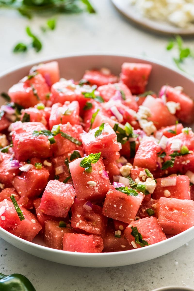 Watermelon salad topped with mint leaves and crumbled feta cheese (or cotija) in a large bowl.