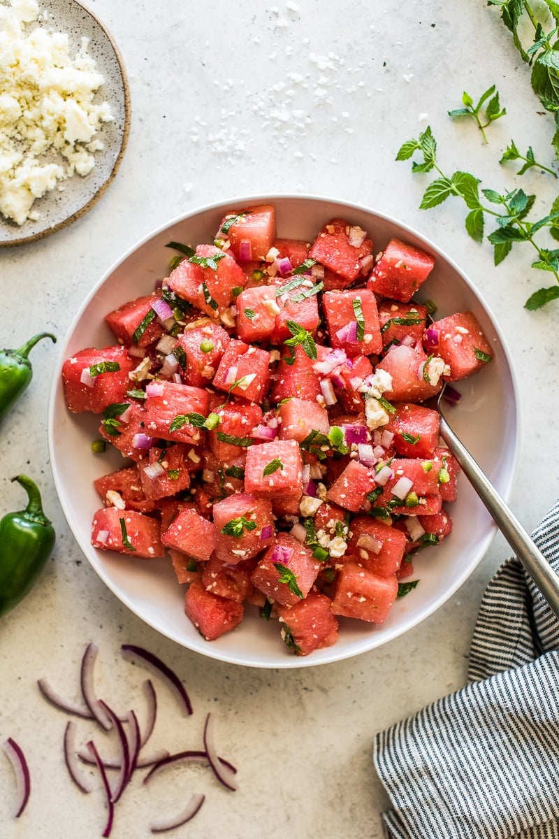 Watermelon salad in a large serving bowl topped with mint leaves, crumbled feta cheese, and red onions.