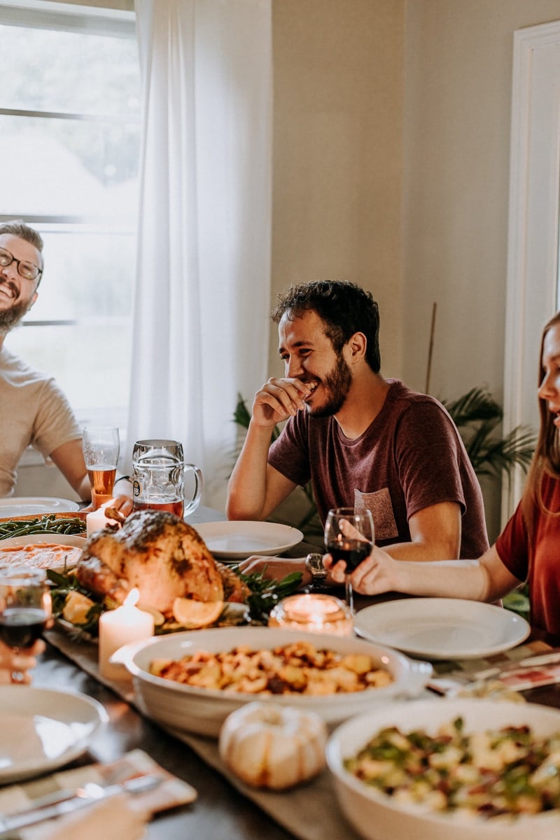 People laughing at a dining room table filled with Thanksgiving food in celebration of Friendsgiving.