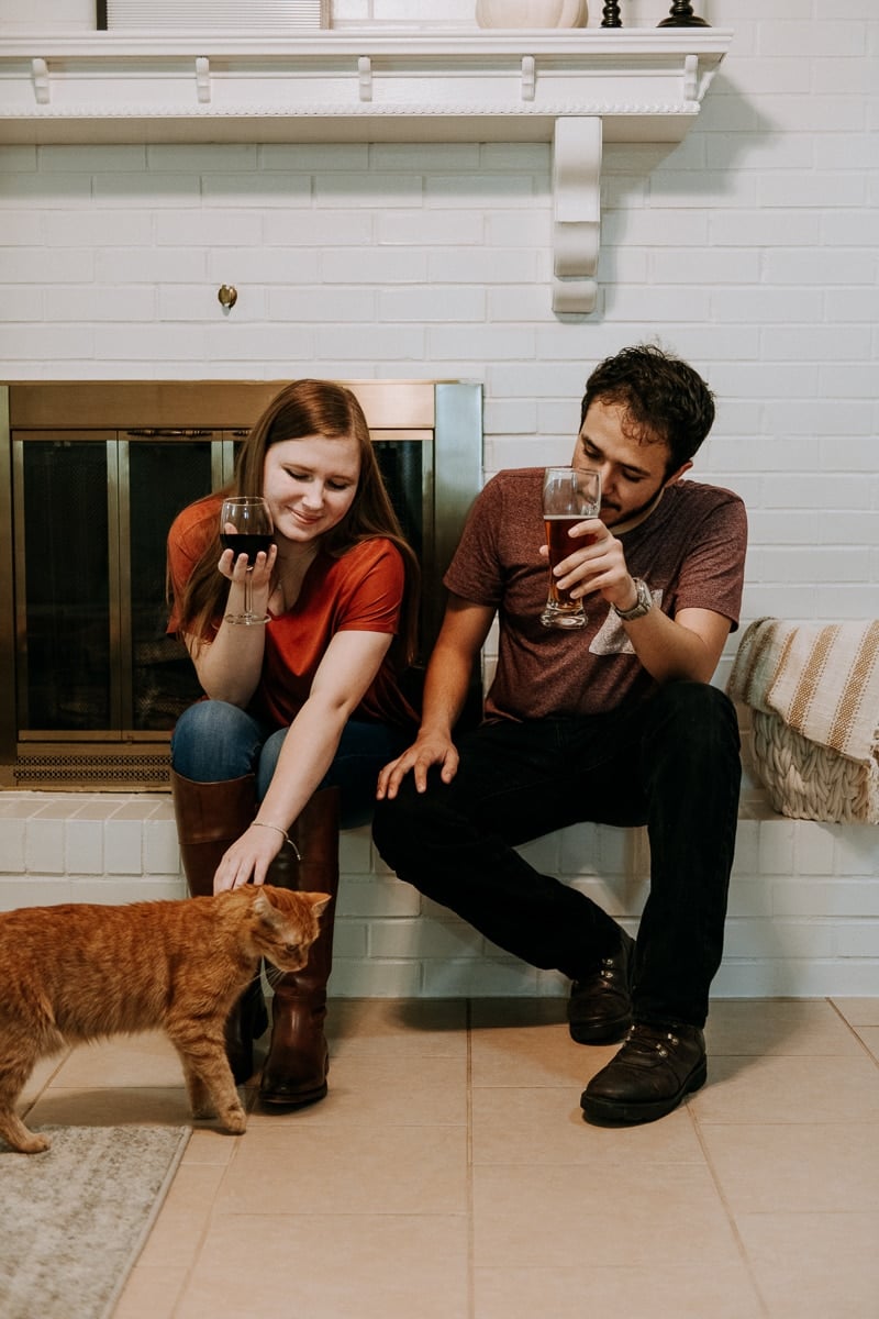 A man and woman sitting by the fireplace petting a cat enjoying Friendsgiving.