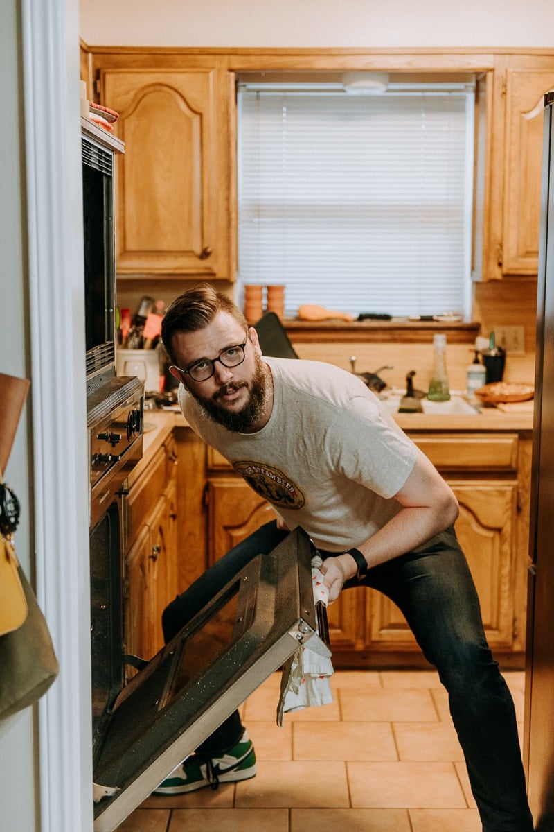 A man posing in front of an oven getting ready to take out a Thanksgiving turkey.